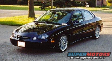 Black 1999 Ford Taurus sedan parked on a driveway, front 3/4 view, with aftermarket wheels