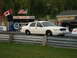 2003 Ford Crown Victoria - White 2003 Ford Crown Victoria at a drag strip, with flags and advertising in the background.
