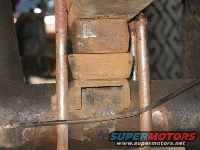 Close-up of rusty rear leaf spring mount with U-bolts and rubber isolators