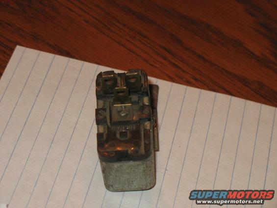 Close-up of an old electrical relay with metal contacts and a grey casing, resting on lined paper