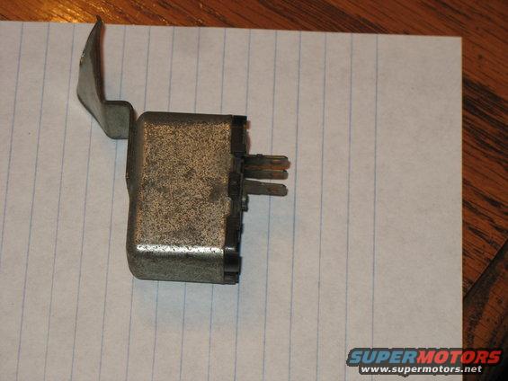 Metal automotive relay with a bracket and electrical pins, resting on lined paper