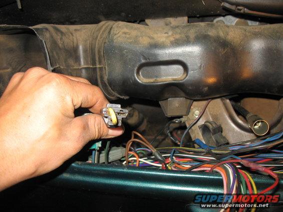 hand disconnecting a yellow and gray electrical connector near a black air duct and a mess of wires