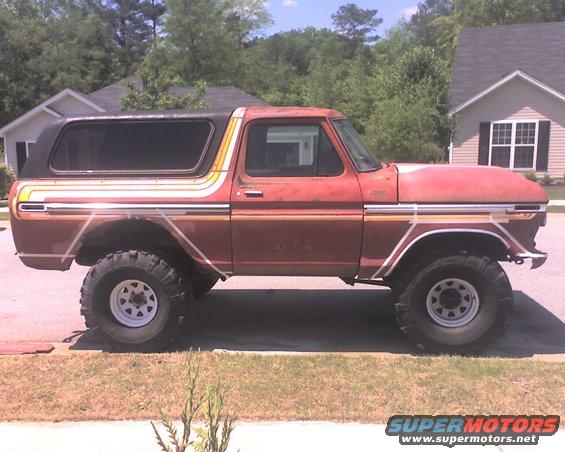 Red 1978 Ford Bronco with black removable top and colorful side stripes, lifted with large tires