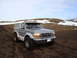 1992 Ford Bronco - A silver 1992 Ford Bronco is parked on a dirt road in a landscape with snow-covered hills.