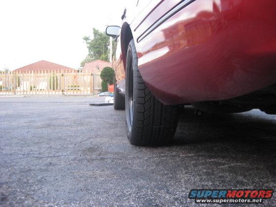 Close-up of a red sedan's rear quarter panel and tire. A wooden fence is in the background