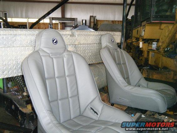 Two grey racing seats with headrests a circular logo
