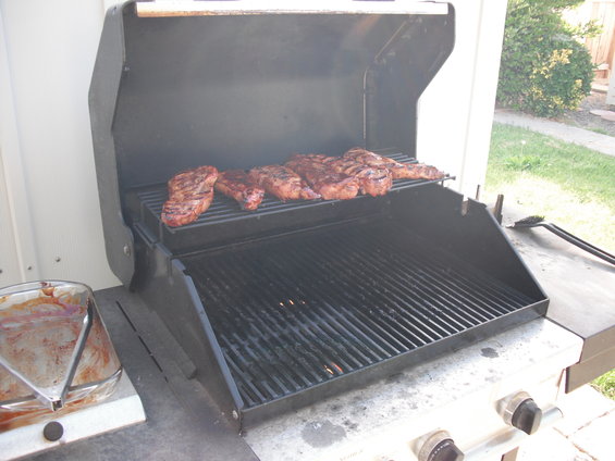 Several steaks cooking on the top rack of a gas grill