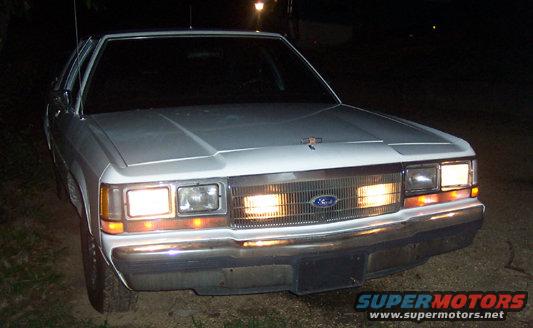 White Ford Crown Victoria with headlights on, front view at night