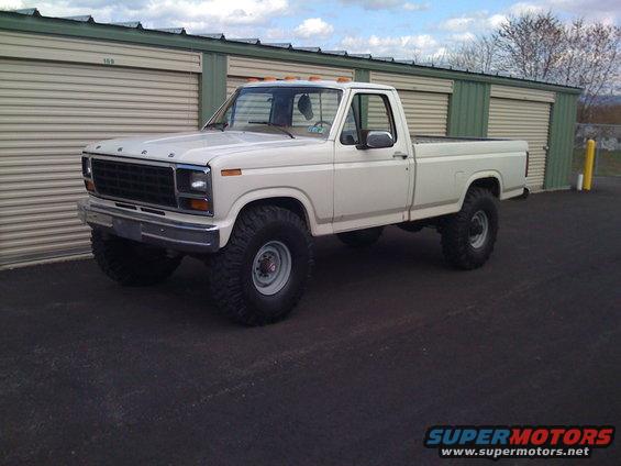 White 1980 Ford F-250 pickup truck with large tires parked in front of storage units