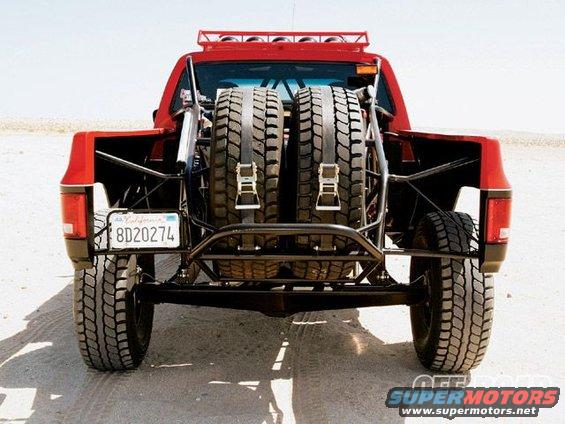 Rear view of a red off-road truck with two spare tires mounted vertically. California license plate reads 8D20274