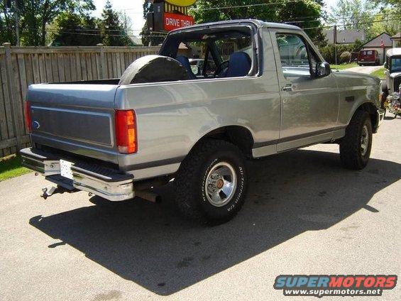 Silver Ford Bronco with removable top, spare tire in bed, parked on asphalt