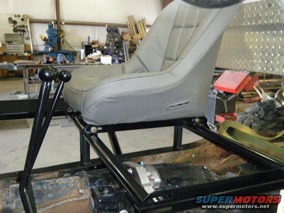 Racing seat and gear shifter in a vehicle interior. Visible text: SUPERMOTORS.NET