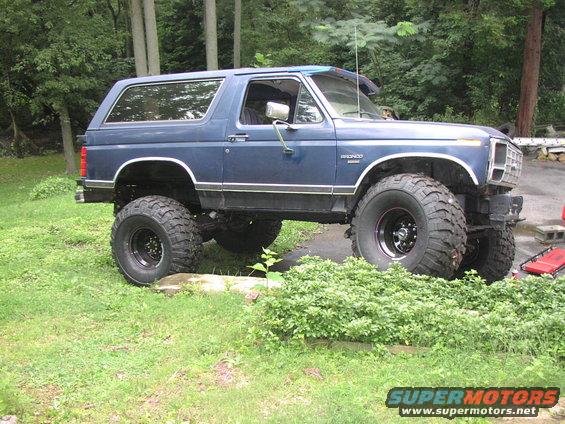 Blue lifted 1986 Ford Bronco parked on grass with trees in background