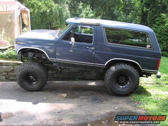 Blue lifted Ford Bronco with off-road tires parked on a driveway, side view