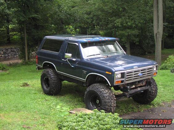 Blue 1986 Ford Bronco with large off-road tires parked on grass