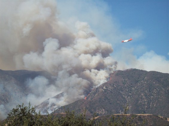 Air tanker flying over a mountain wildfire, dropping retardant