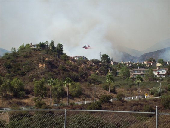 Firefighting plane dropping red retardant over a smoky hillside with houses