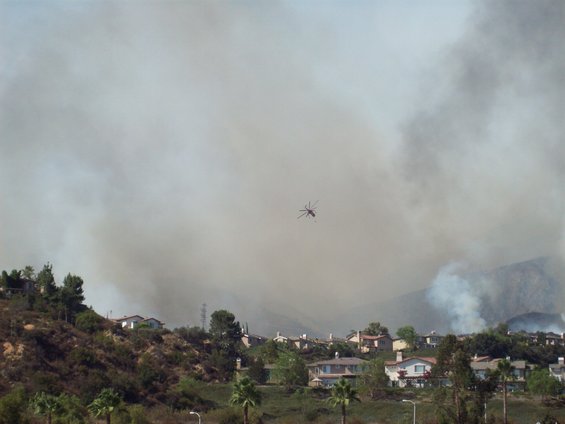 Helicopter flies over residential area with heavy smoke and flames visible