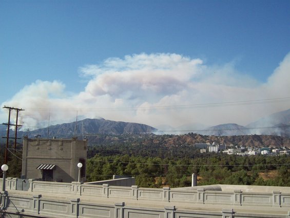 Wildfire smoke billows over mountains and a town under a blue sky