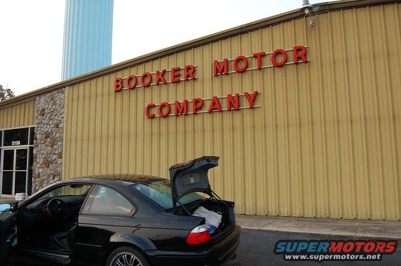 Black coupe with trunk open parked outside Booker Motor Company. The car looks like a BMW M3