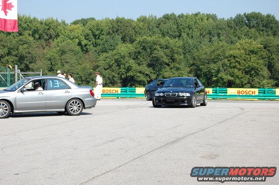 Black BMW M3 with front damage on a race track, viewed from the front-right