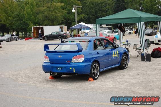 Blue Subaru WRX STI with a large rear spoiler and racing numbers on the door, parked on a gravel surface