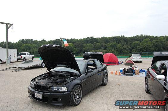 Black 2002 BMW M3 with hood open, parked at a track with tents and other cars around