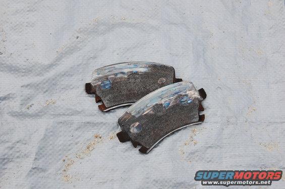 Two worn brake pads on a white cloth. Supermotors.net logo visible