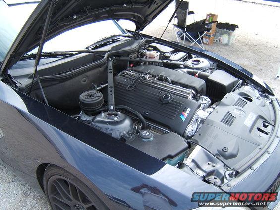Engine bay of a dark blue BMW with the hood up. The M logo is visible on the engine cover
