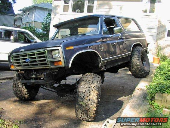 Lifted dark blue 1980s Ford Bronco with large tires, front 3/4 view