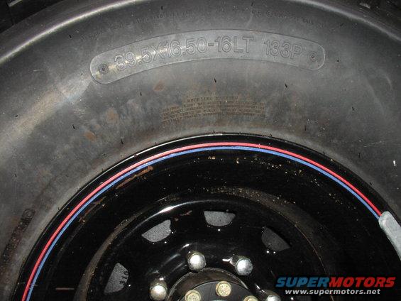 Close-up of a tire with size 39.5x16.50-16LT 133P and a black wheel with red and blue trim