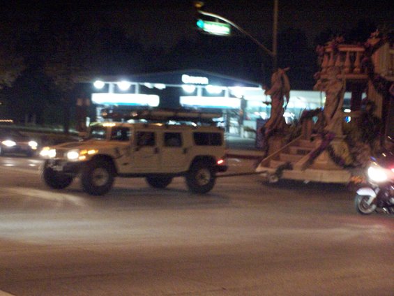 Hummer H1 towing a float at night, with a motorcycle visible on the right