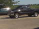 2005 Ford F-250 - A black Ford F-250 pickup truck is parked on a paved surface with a field and trees in the background.