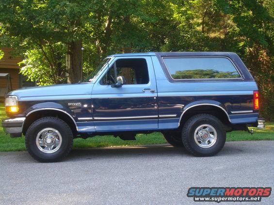 Blue two-tone 1992 Ford Bronco side view, chrome trim, alloy wheels, parked on asphalt