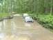 1993 Jeep Cherokee - Multiple off-road vehicles navigate a flooded dirt path surrounded by dense forest.