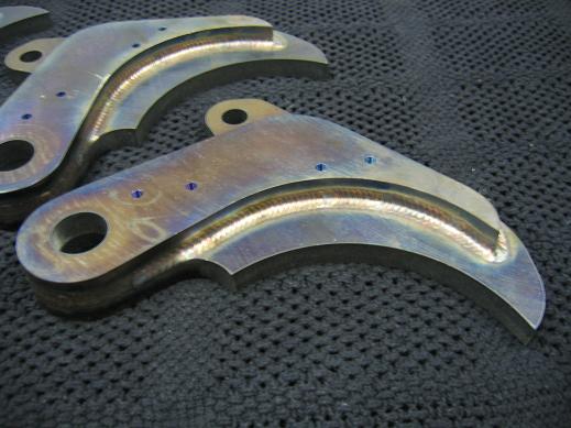 Two welded metal brackets with blue scribe marks on a dark textured surface