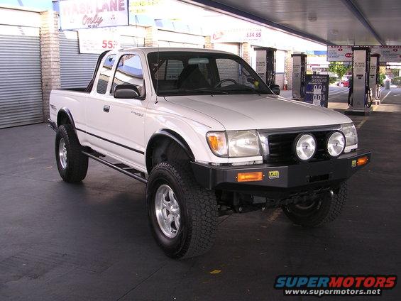 White Toyota pickup truck with aftermarket bumper and lights, parked at a gas station