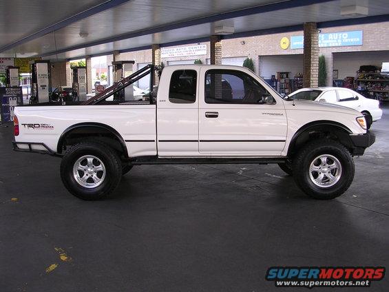 White 1999 Toyota Tacoma TRD pickup truck with aftermarket roll bar, parked at a gas station