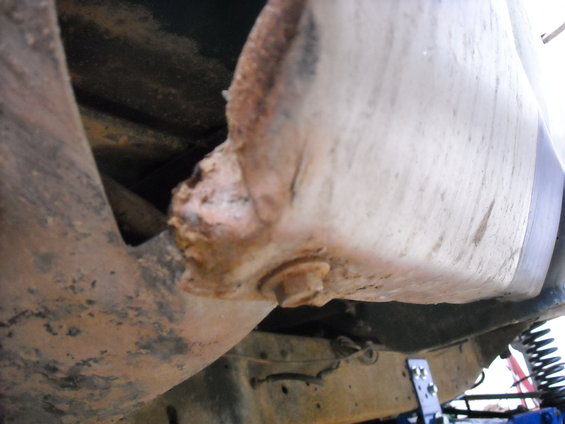 Close-up of heavily rusted metal frame and underside of a vehicle body panel, showing corrosion and a bolt