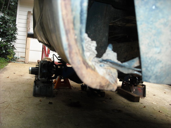 Close-up of heavily rusted vehicle frame and rear axle assembly supported by jack stands
