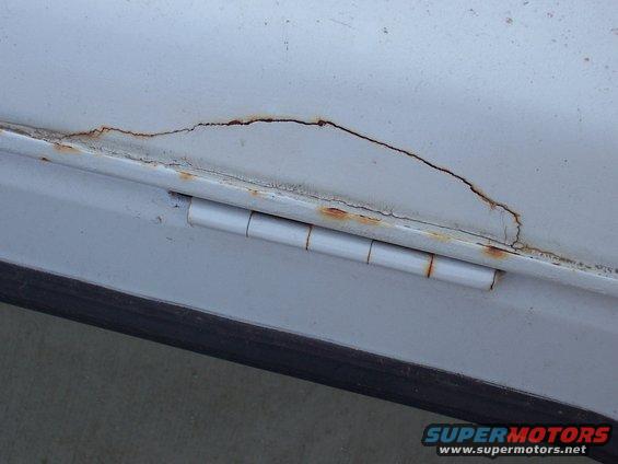 close-up of a white door hinge with rust and cracks in the paint