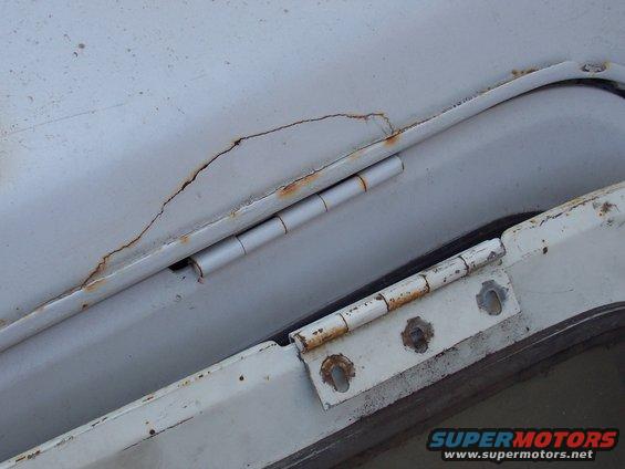 Rusted hinge on a white vehicle part with visible cracks