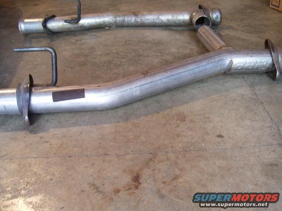 Exhaust pipes with hangers on a concrete floor. One pipe has a dark rectangular sticker