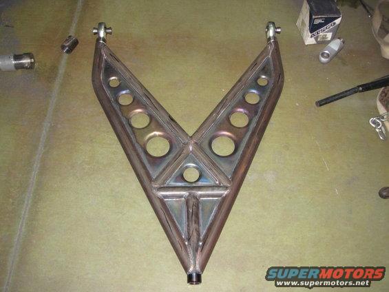 Custom V-shaped metal suspension component with circular cutouts, resting on a workbench next to a box and some tools