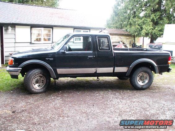 Black 1990s Ford Ranger pickup truck, side view, parked on gravel in front of a house