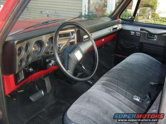Interior of a red truck, showing the dashboard, steering wheel, and bench seat