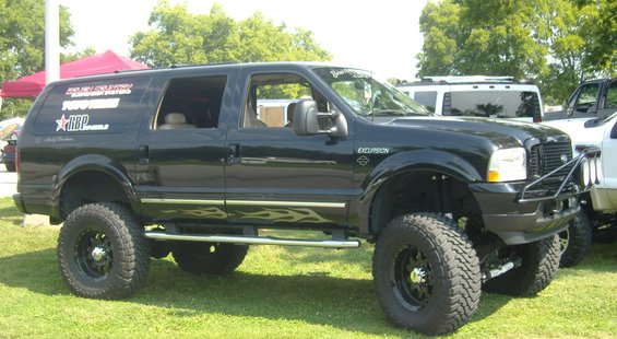Black SUV with flame decals on the side, lifted with large tires, parked on grass