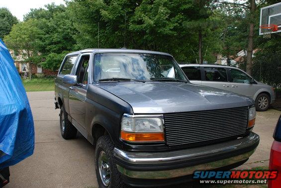 Gray Ford Bronco with aftermarket grille, parked in driveway next to a silver minivan