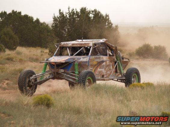 Off-road buggy with green suspension and rusty body, kicking up dust