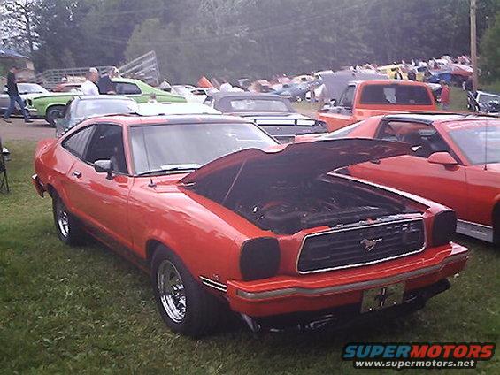 Red coupe with hood open, parked on grass at an outdoor car show